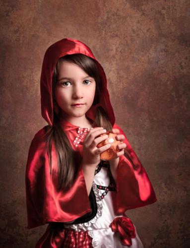 Studio portrait of a young girl wearing Little Red riding hood costume. She is holding a red apple and looking at the camera. 
